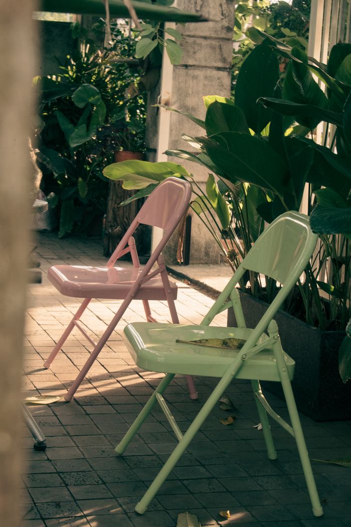 Home Pink and green folding chairs in a sunny garden with lush plants.