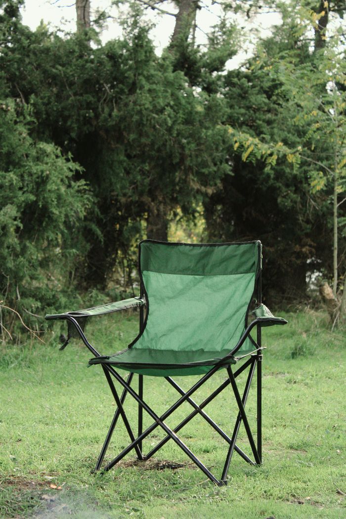 Home A green folding camping chair sits in a verdant forest clearing, evoking tranquility.