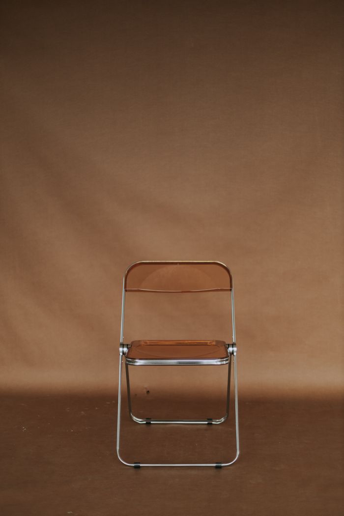 Home A minimalist brown folding chair set against a brown studio backdrop, ideal for design concepts.