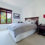 Home A stylish and comfortable bedroom interior featuring a wooden bed and nightstand with a red lamp and large window.