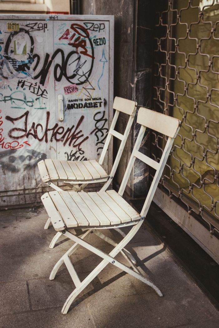 Home Pair of white folding chairs on urban street with graffiti backdrop.