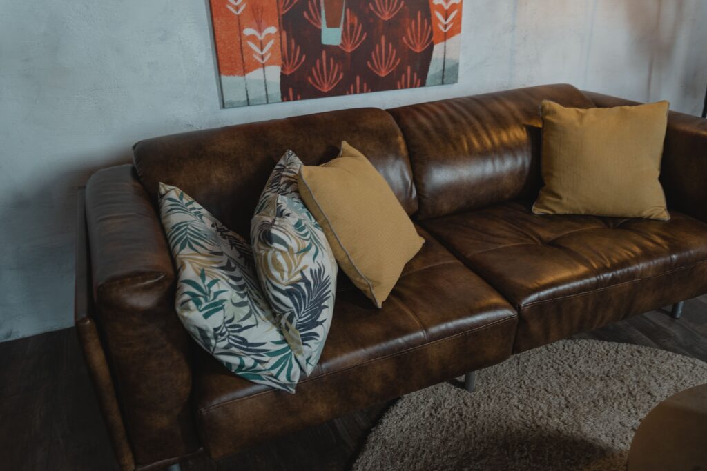 Warm brown leather sofa with patterned and plain pillows in a cozy living room setting.