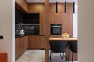 Modern kitchen interior with wooden furniture and dining table with vase of fresh fruits in stylish apartment