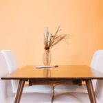 Home Table with glass vase with various flowers and plants near chairs in light room with yellow wall