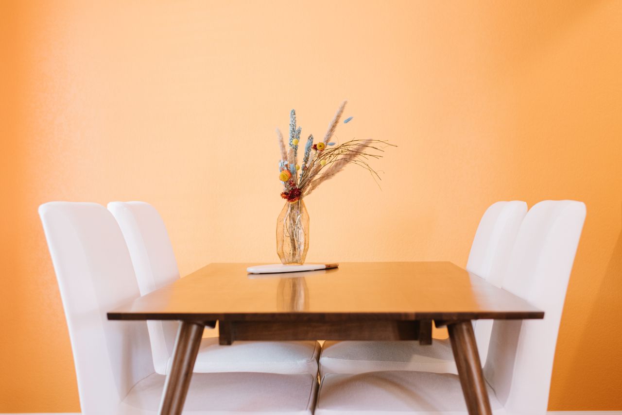Table with glass vase with various flowers and plants near chairs in light room with yellow wall