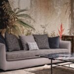 Home Comfortable sofa with pillows placed at wall with painted leaves in modern spacious room with table on rug at home