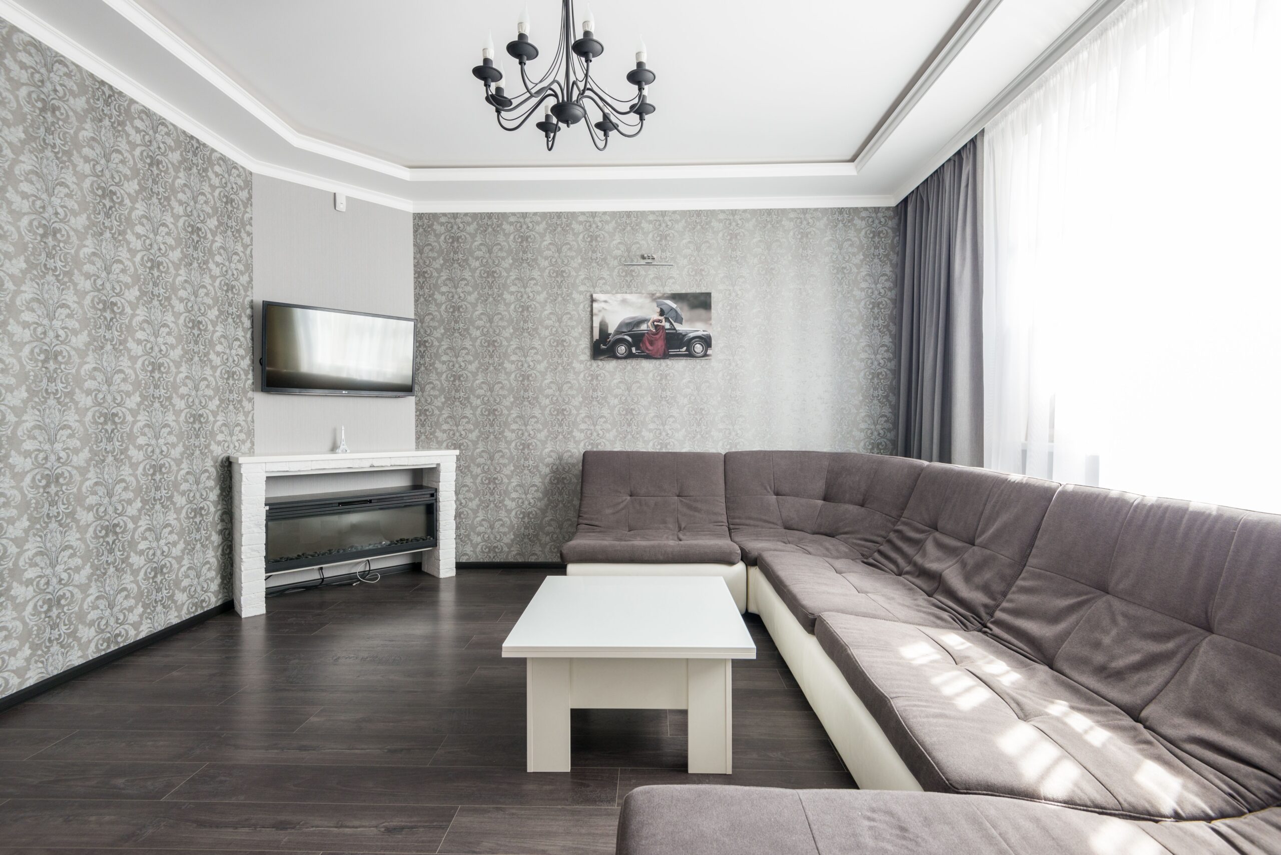 Home Spacious modern living room featuring a comfortable sofa, chic wallpaper, and a stylish chandelier.