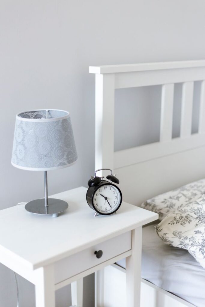 Elegant minimalist bedroom showcasing a bedside table with alarm clock and modern lamp.