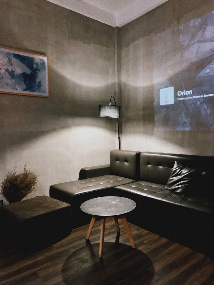 Interior of modern apartment with comfortable leather sofa placed in corner near wall with projection and round table near sofa lit by floor lamp